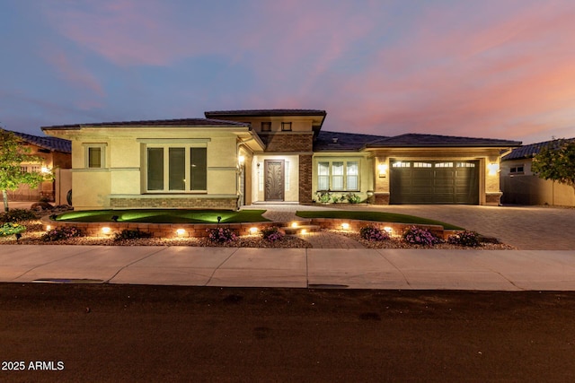 prairie-style home featuring decorative driveway, an attached garage, and stucco siding