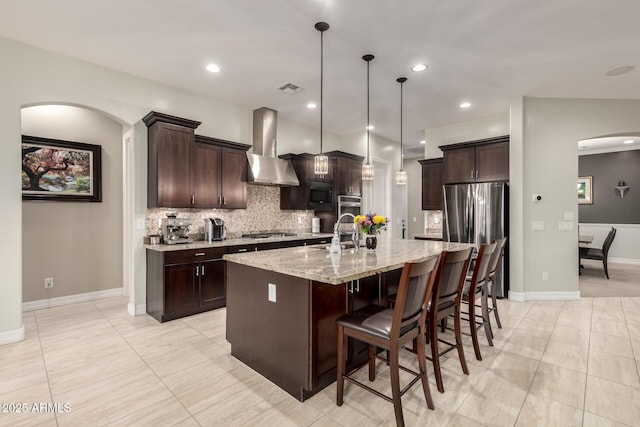 kitchen with a kitchen island with sink, visible vents, dark brown cabinets, wall chimney range hood, and appliances with stainless steel finishes