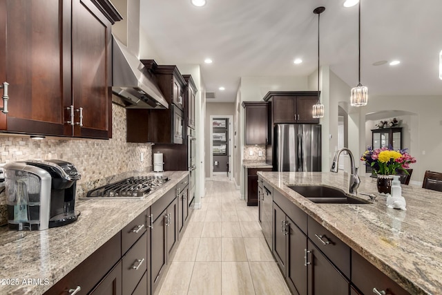 kitchen featuring arched walkways, light stone counters, appliances with stainless steel finishes, extractor fan, and a sink