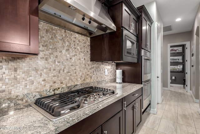 kitchen with light stone counters, stainless steel appliances, decorative backsplash, ventilation hood, and dark brown cabinets