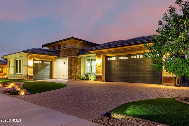 prairie-style home featuring a garage, brick siding, decorative driveway, and stucco siding