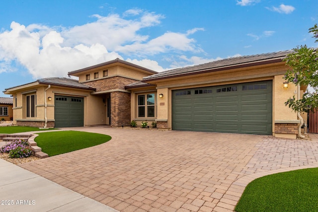 prairie-style house with a garage, brick siding, decorative driveway, and stucco siding