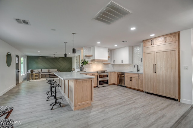 kitchen featuring kitchen peninsula, light brown cabinetry, appliances with stainless steel finishes, sink, and pendant lighting