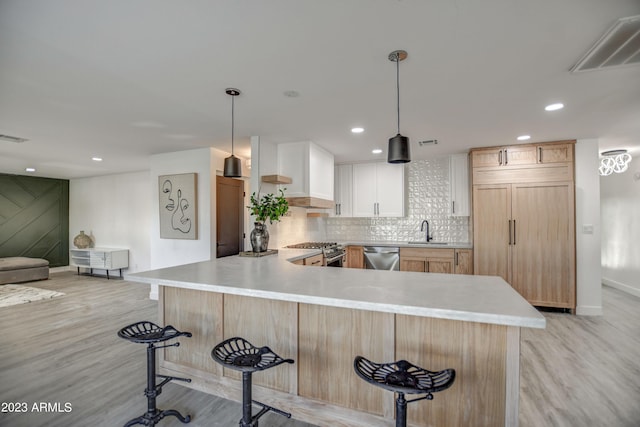 kitchen with high end appliances, white cabinets, sink, decorative light fixtures, and kitchen peninsula