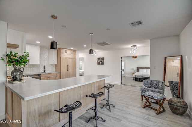 kitchen featuring white cabinetry, sink, hanging light fixtures, kitchen peninsula, and light wood-type flooring