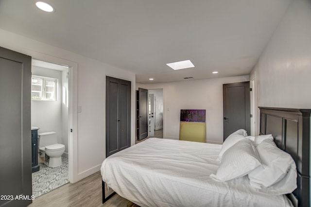 bedroom featuring connected bathroom, a skylight, and light wood-type flooring