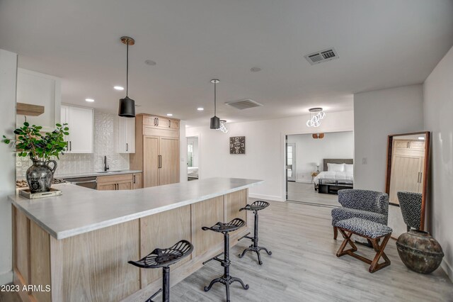 kitchen with sink, hanging light fixtures, kitchen peninsula, white cabinets, and light wood-type flooring