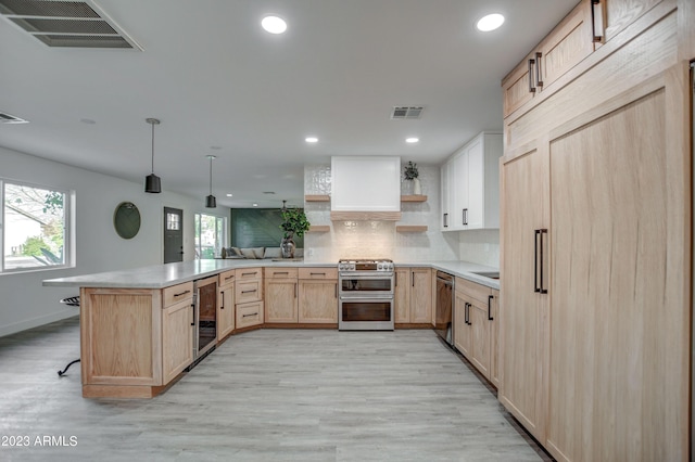 kitchen with light brown cabinets, light wood-type flooring, appliances with stainless steel finishes, kitchen peninsula, and beverage cooler