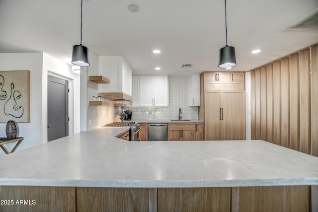 kitchen featuring sink, premium appliances, kitchen peninsula, pendant lighting, and white cabinets