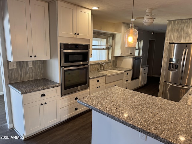 kitchen with appliances with stainless steel finishes, pendant lighting, white cabinetry, sink, and dark wood-type flooring