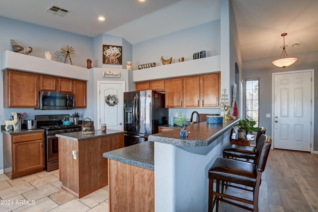 kitchen with kitchen peninsula, light hardwood / wood-style floors, decorative light fixtures, a breakfast bar, and appliances with stainless steel finishes