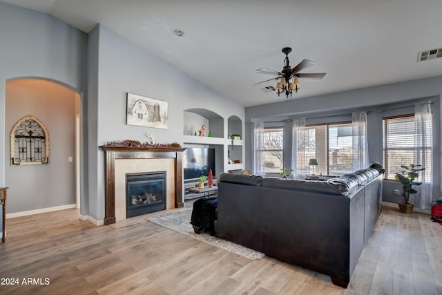 living room featuring ceiling fan, vaulted ceiling, a tile fireplace, and light hardwood / wood-style flooring