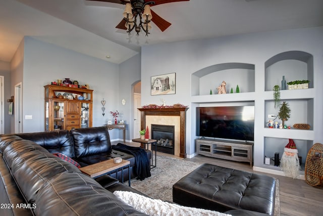 living room with built in shelves, ceiling fan, a tile fireplace, light hardwood / wood-style floors, and lofted ceiling