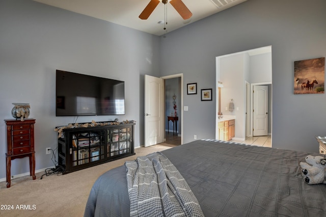 bedroom with ceiling fan, ensuite bathroom, a towering ceiling, and light colored carpet