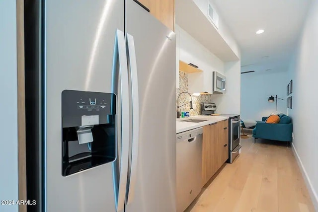 kitchen with light brown cabinets, sink, decorative backsplash, light wood-type flooring, and appliances with stainless steel finishes