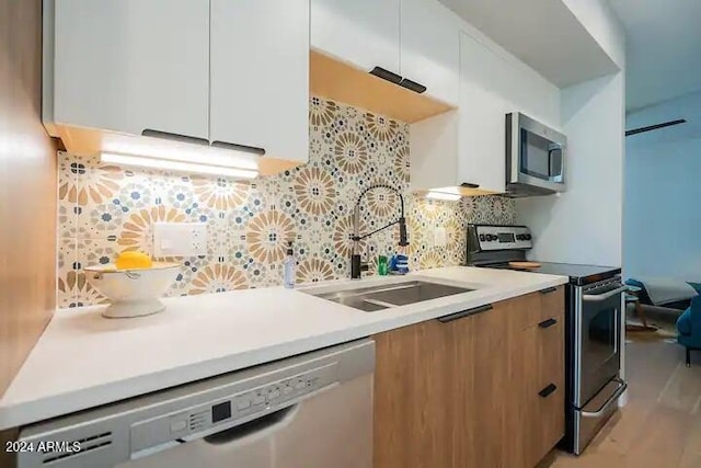 kitchen with decorative backsplash, appliances with stainless steel finishes, sink, white cabinets, and light hardwood / wood-style floors