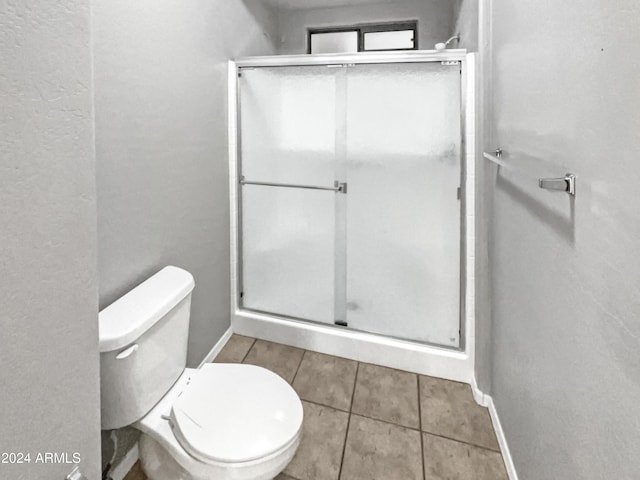 bathroom featuring tile patterned floors, toilet, and a shower with door