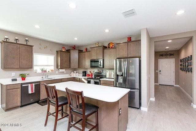 kitchen with a kitchen bar, appliances with stainless steel finishes, sink, light hardwood / wood-style flooring, and a kitchen island