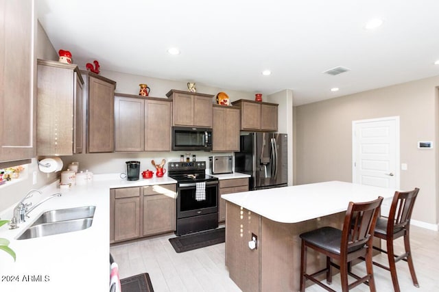 kitchen with a breakfast bar, a center island, sink, light wood-type flooring, and appliances with stainless steel finishes