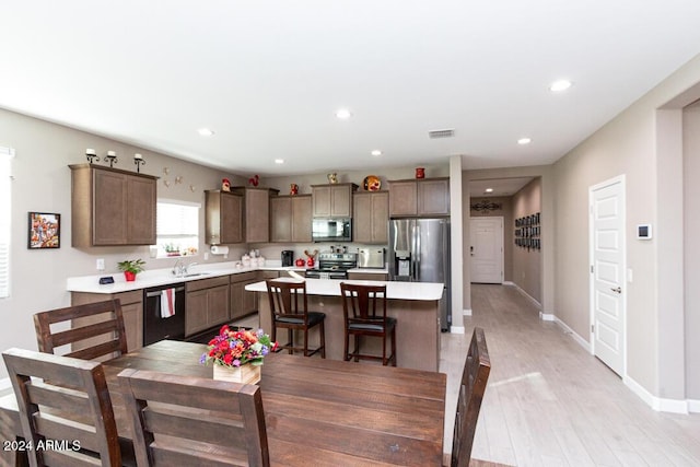 kitchen with appliances with stainless steel finishes, sink, light hardwood / wood-style flooring, a kitchen island, and a breakfast bar area