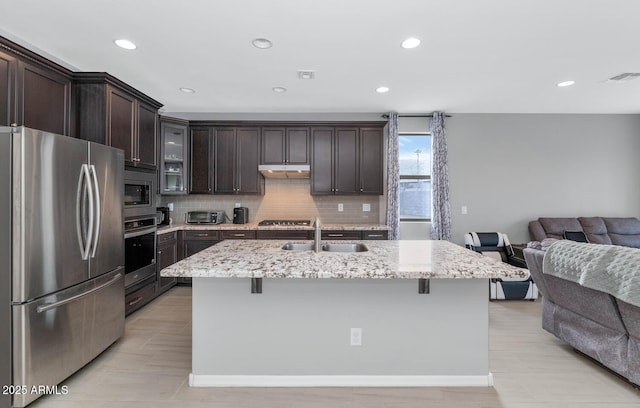 kitchen with light stone countertops, a kitchen island with sink, and appliances with stainless steel finishes