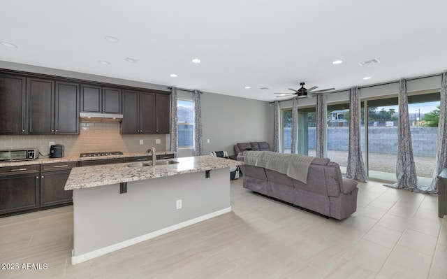 kitchen with a center island with sink, sink, ceiling fan, gas stovetop, and a kitchen bar