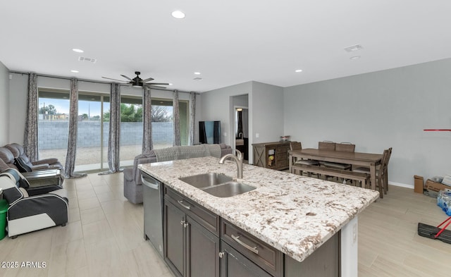 kitchen with dishwasher, light stone counters, sink, and an island with sink