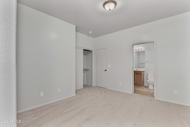 unfurnished bedroom with ensuite bathroom, a closet, and light colored carpet