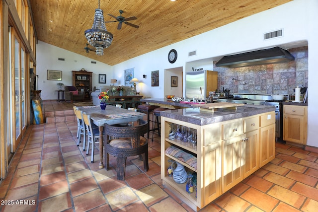 kitchen featuring wood ceiling, dark countertops, wall chimney range hood, ceiling fan with notable chandelier, and visible vents