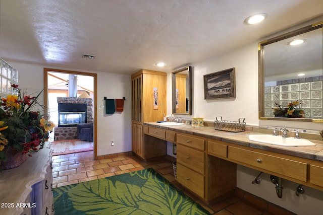 bathroom featuring visible vents, recessed lighting, a sink, and a brick fireplace