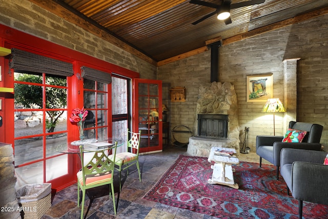 living area featuring stone tile floors, brick wall, vaulted ceiling, and ceiling fan