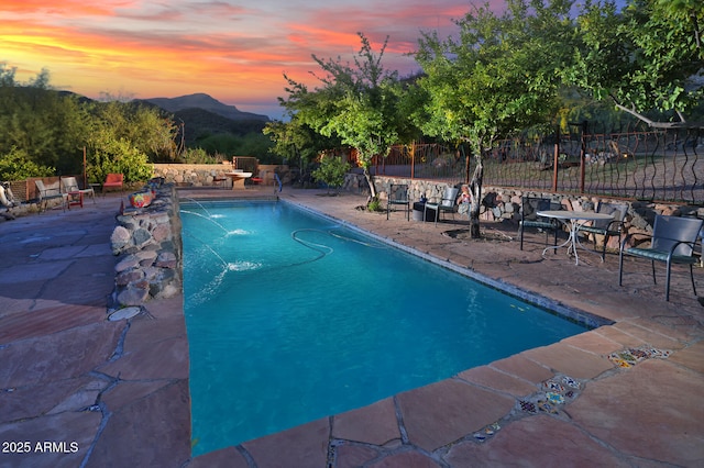 pool at dusk with a fenced in pool, a mountain view, fence, and a patio