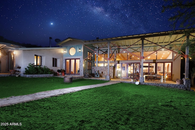 back of house at night featuring a lawn