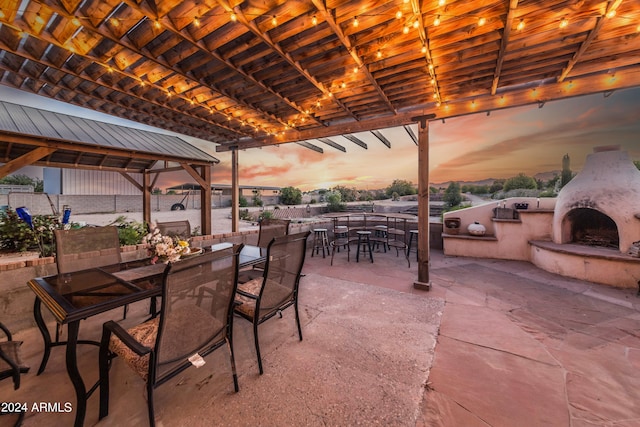 patio terrace at dusk featuring a gazebo and exterior fireplace