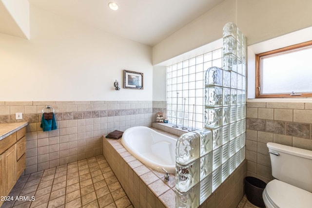 bathroom featuring a tub to relax in, tile patterned floors, vanity, tile walls, and toilet