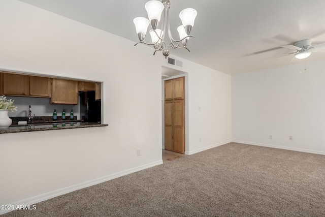 interior space with black refrigerator, ceiling fan with notable chandelier, dark stone counters, hanging light fixtures, and light colored carpet