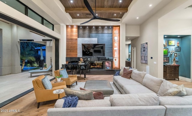 living area with beamed ceiling, light wood-type flooring, a glass covered fireplace, and recessed lighting