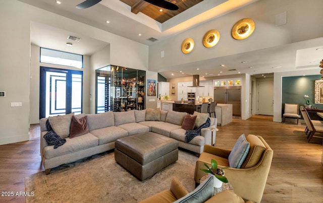 living area featuring ceiling fan, a high ceiling, visible vents, baseboards, and light wood finished floors