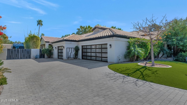 mediterranean / spanish house with a front lawn, decorative driveway, an attached garage, and a tile roof