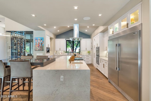 kitchen with stainless steel appliances, a spacious island, light stone countertops, and white cabinets