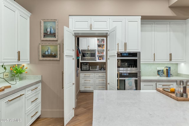 kitchen with light wood finished floors, tasteful backsplash, baseboards, white cabinets, and stainless steel appliances