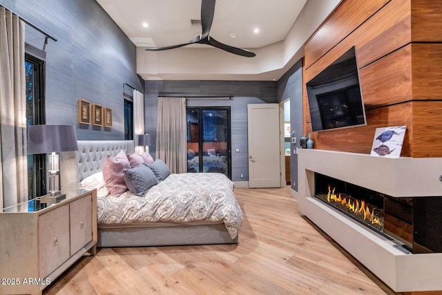 bedroom featuring recessed lighting, light wood-style floors, a ceiling fan, access to outside, and a warm lit fireplace