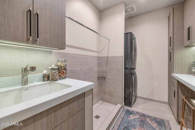 full bath with stacked washer and dryer, visible vents, decorative backsplash, vanity, and tile patterned flooring