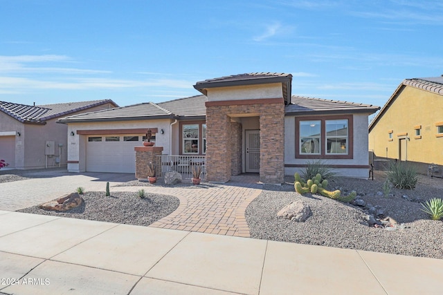prairie-style house with a garage, driveway, stone siding, a tiled roof, and stucco siding