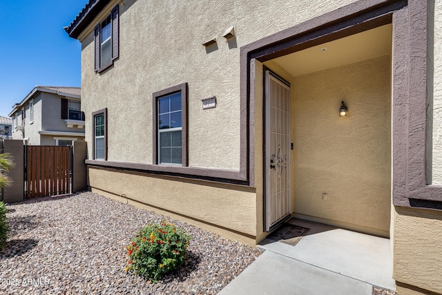 view of exterior entry with stucco siding and fence