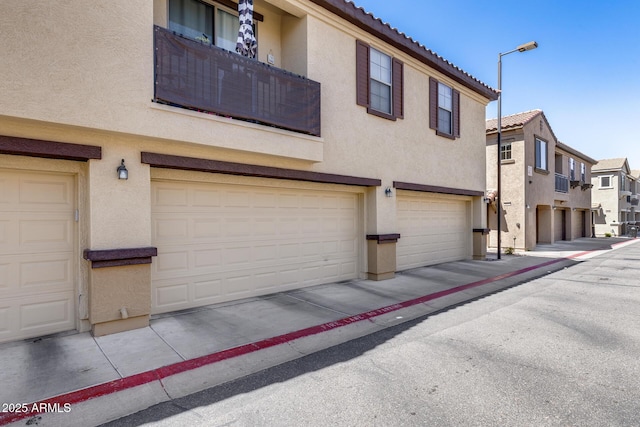 exterior space with an attached garage, stucco siding, a tiled roof, and a residential view