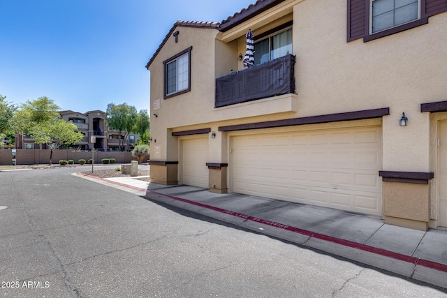 view of property exterior with a garage, fence, stucco siding, and a balcony
