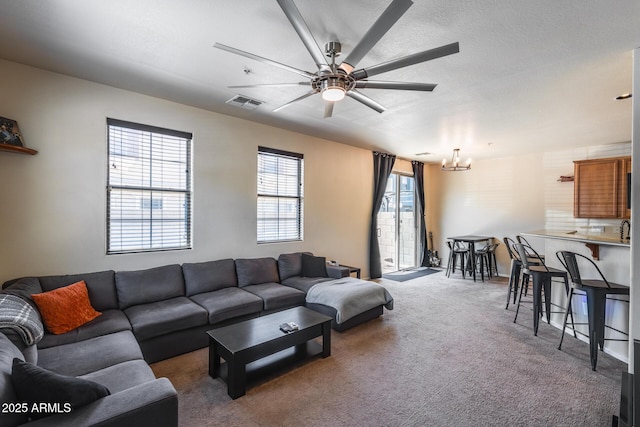 carpeted living area featuring ceiling fan with notable chandelier and visible vents