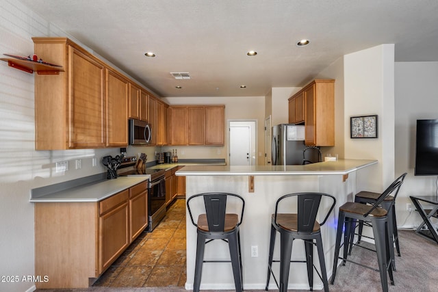 kitchen featuring visible vents, a peninsula, a kitchen breakfast bar, light countertops, and stainless steel appliances