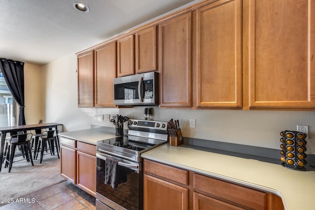 kitchen featuring light colored carpet, light countertops, a textured ceiling, and stainless steel appliances